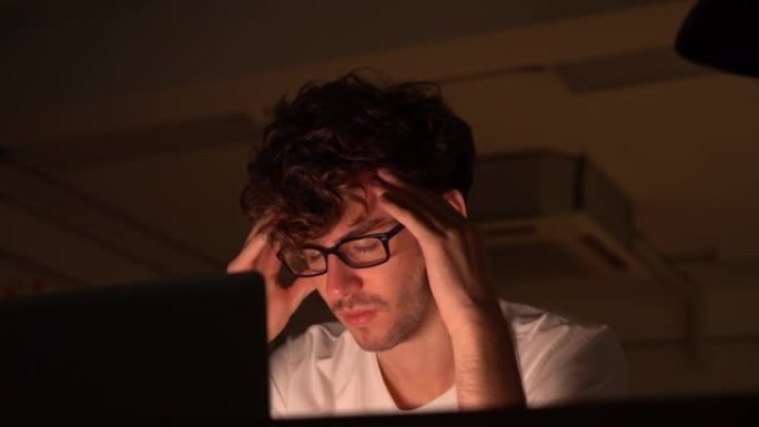 疲惫的男人双手坐在笔记本电脑前，压力很大，晚上工作得筋疲力尽。