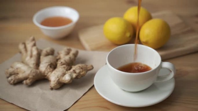 将香茶倒入白色杯子中。生姜，柠檬，蜂蜜和凉茶放在木桌上。