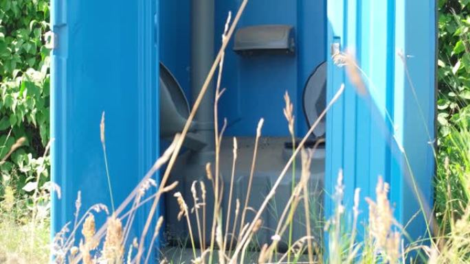 露天音乐节期间，蓝色塑料移动公共厕所厕所站在高草草地中间