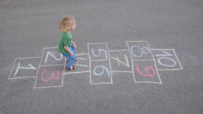小男孩的腿和跳房子画在沥青上。春天的孩子在操场上玩跳房子游戏。儿童户外活动。