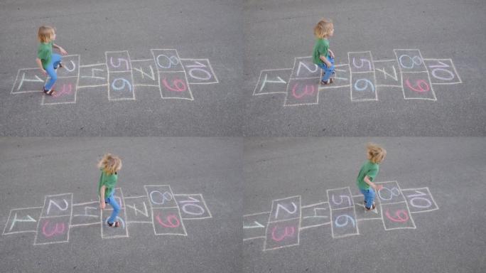 小男孩的腿和跳房子画在沥青上。春天的孩子在操场上玩跳房子游戏。儿童户外活动。