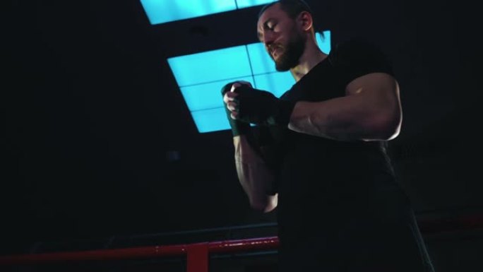 拳击手站在黑暗的健身房里，手腕上缠着绷带