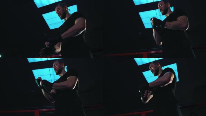 拳击手站在黑暗的健身房里，手腕上缠着绷带