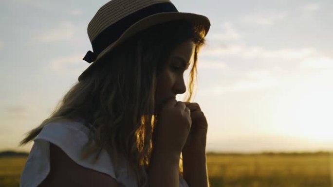 一个戴着帽子的女孩在日落时在田野里吃大自然的水果。它被凉爽的夜光照亮。