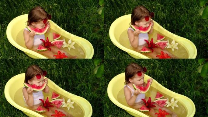 一个可爱的小女孩沐浴在黄色的水浴中，在自然界中花和鸭子，并吃多汁的甜西瓜