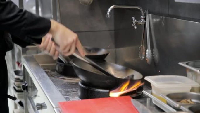 厨师的手将锅中的钢包油倒在煤气炉火焰上，以在烹饪前将其加热