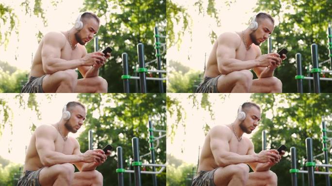 肌肉发达的人坐在城市公园的运动场上，一边看音乐一边看手机