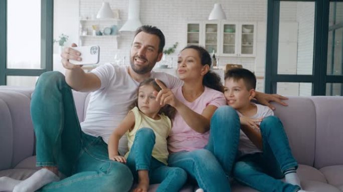 成熟的父亲，丈夫坐在他漂亮的妻子和孩子旁边，拿着手机，通过视频通话召开家庭视频会议。家人挥手看手机屏