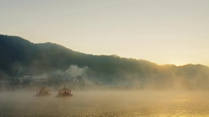 泰国湄宏顺的Ban Rak Thai村的河流湖上的传统中式船，早晨雾蒙蒙，背景是阳光日出山