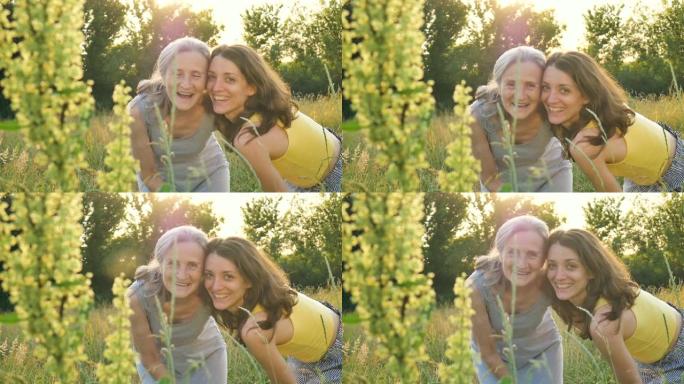 年老的母亲，头发花白，成年的女儿看着花园里的相机，在户外阳光明媚的日子里互相拥抱，母亲节