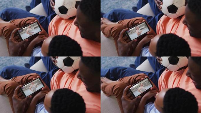 父亲和儿子在智能手机上在家观看田径比赛的合成