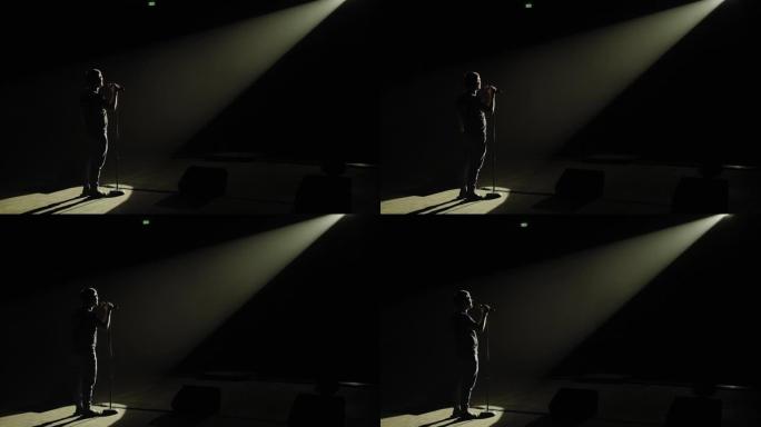 一个男人在黑暗中拿着麦克风在舞台上的剪影。