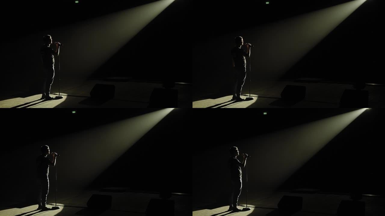 一个男人在黑暗中拿着麦克风在舞台上的剪影。
