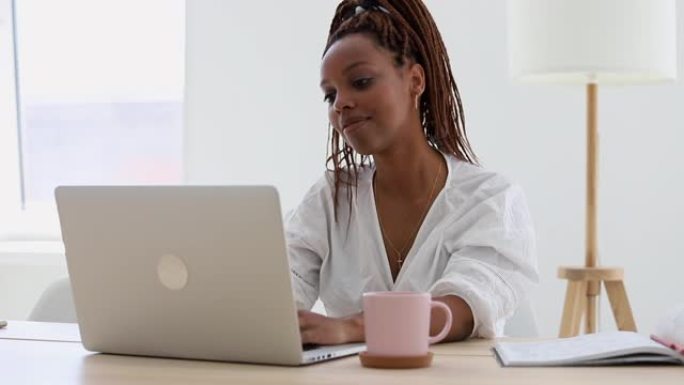女人带着微笑在笔记本电脑上工作。美国黑人妇女在家庭办公室学习。学院