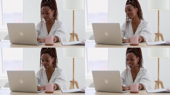 女人带着微笑在笔记本电脑上工作。美国黑人妇女在家庭办公室学习。学院