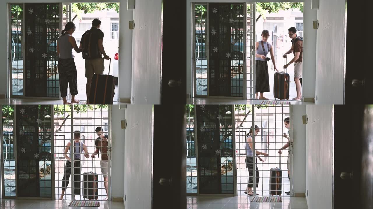年轻的亚洲夫妇站在前门，手提箱正要去度假
