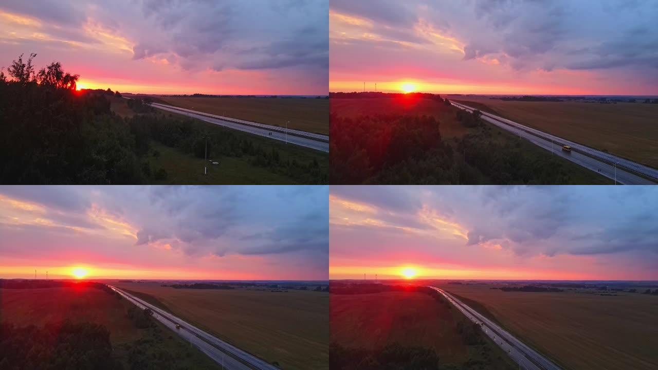 红色日落时高速公路的全景鸟瞰图。乡村田野附近有道路的景观。美丽的蜿蜒小路通向傍晚的乡村。戏剧性的天空