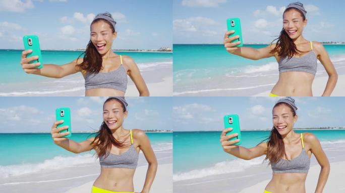 快乐的运动女孩在沙滩上跑步后笑着用手机自拍。女人在暑假锻炼后进行健身自拍，过着健康的生活方式。红色慢