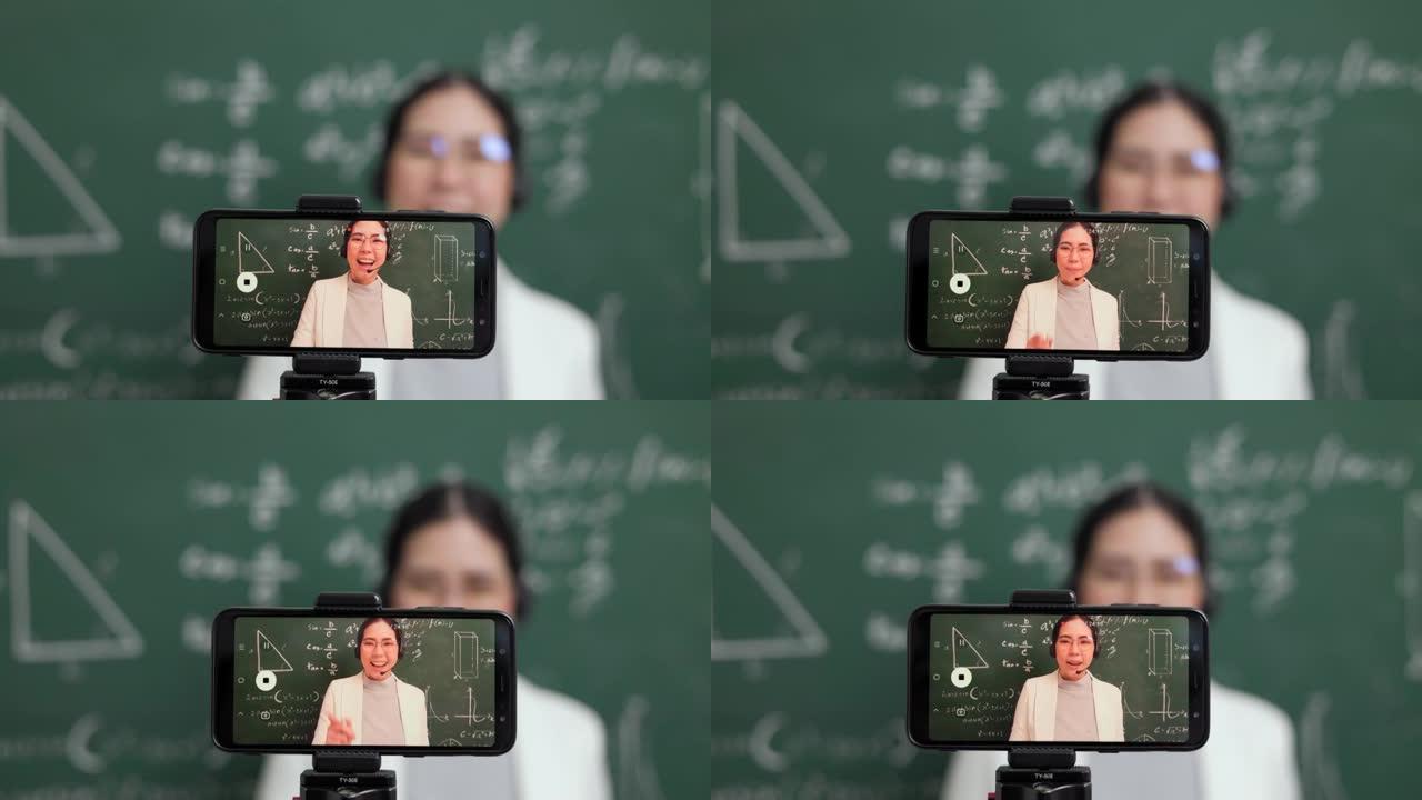 年轻的亚洲教师妇女站在与学生的摄像机和视频会议上。女教师通过智能手机在线课程从直播中培训课堂数学。