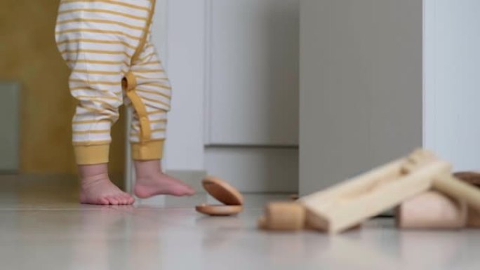 小婴儿赤脚走在地板上，玩具散落在家里。儿童玩耍迈出第一步