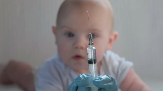 儿科医生为新生儿接种疫苗。疫苗，婴儿疫苗护士手中柔软的聚焦注射器和婴儿背景模糊的白色婴儿。戴着蓝色手