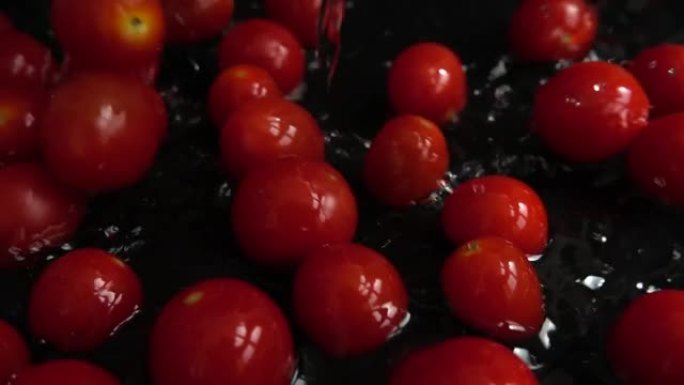 把红色的樱桃西红柿掉进水里。洗西红柿。在黑色背景上。慢动作。