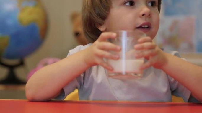 母亲为儿子倒出一杯牛奶。慢动作。特写。小男孩微笑着，早餐喝牛奶。特写。快乐的孩子男孩吃健康的食物。