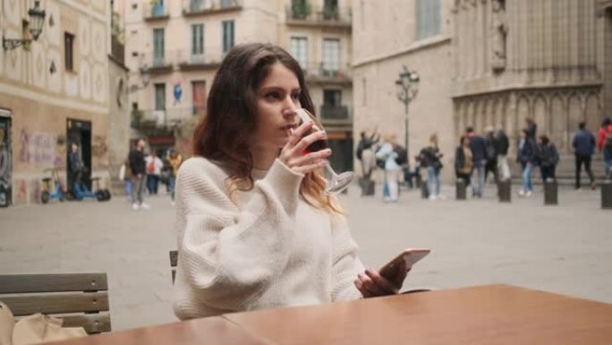 美丽的休闲西班牙裔女孩，智能手机在舒适的街道上喝葡萄酒和做梦