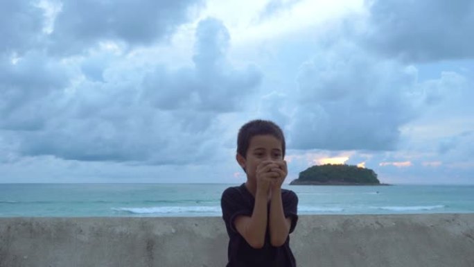日落时分，泰国普吉岛卡塔海滩，一个男孩在海边的墙边滚动一个玻璃球。