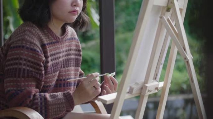 年轻的亚洲女画家在后院用画笔和画架创作艺术品。