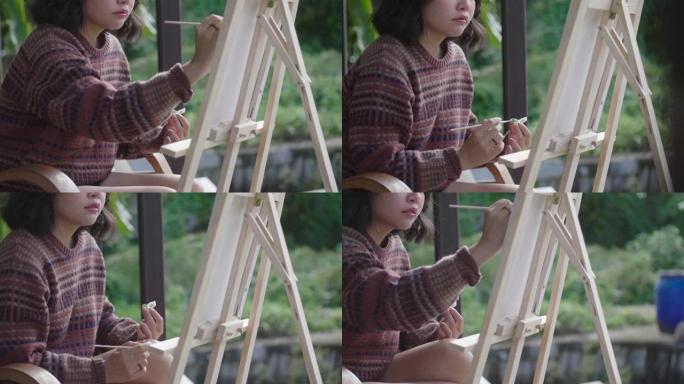 年轻的亚洲女画家在后院用画笔和画架创作艺术品。