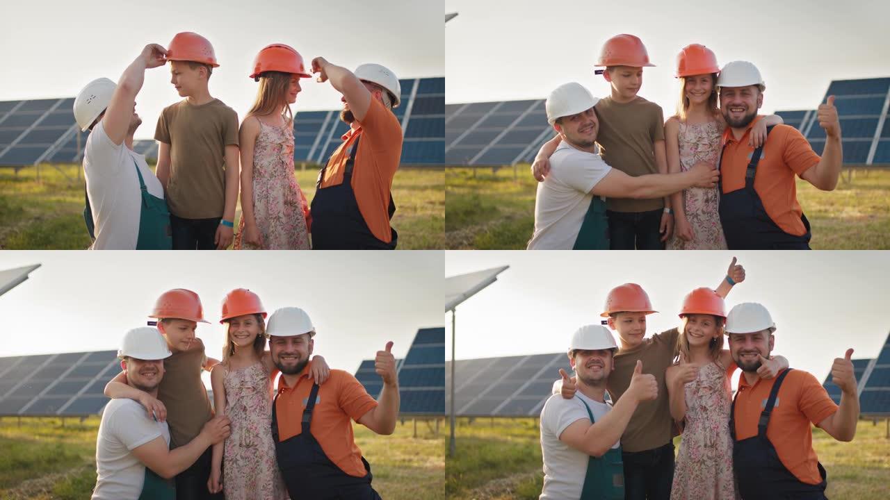 在太阳能发电厂，两个爸爸和两个戴着防护头盔的孩子的肖像，都指着相机并微笑着。父母在太阳能发电厂将头盔