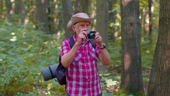 资深男子祖父在徒步旅行中探索野生动物，用复古相机在森林里拍照