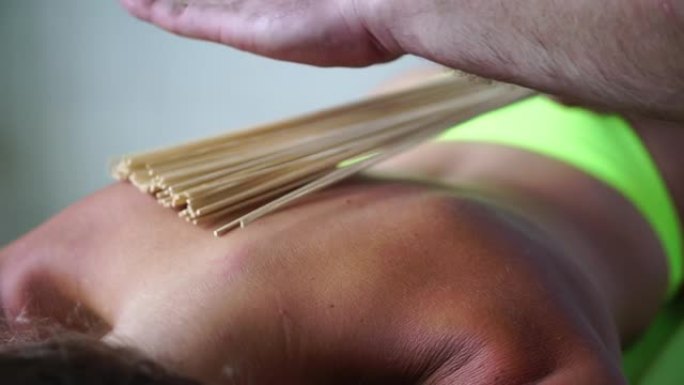 水疗护理用竹扫帚抗脂肪团按摩。治疗师用竹棍按摩女人的背部，以帮助包裹和最有效的引流按摩
