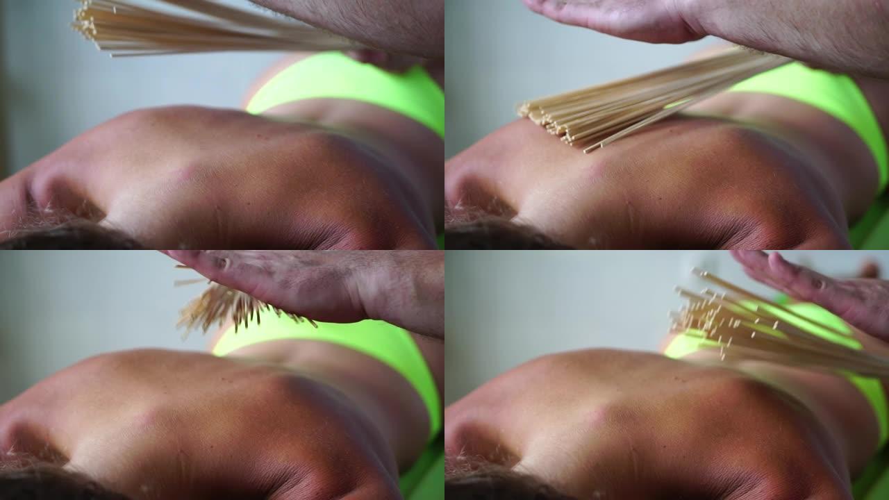 水疗护理用竹扫帚抗脂肪团按摩。治疗师用竹棍按摩女人的背部，以帮助包裹和最有效的引流按摩