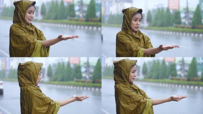 年轻疲惫的女上班族穿着黄色雨衣，被雨水卡住，站在屋顶下，用手玩耍收集雨滴，季风造成的大雨，亚洲城市生