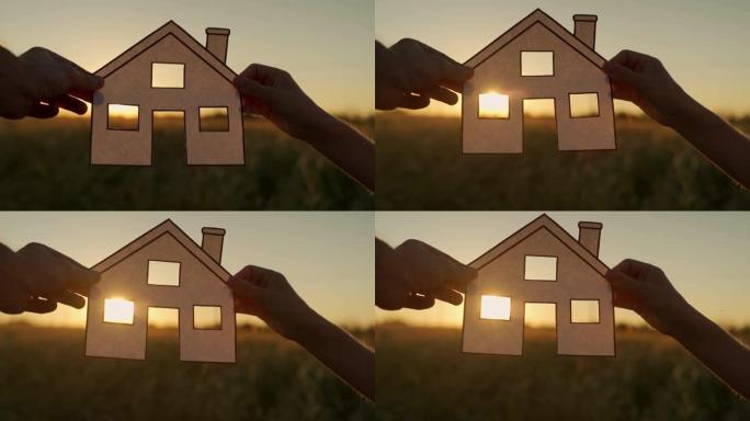 家人在日落时拿着纸房子，阳光透过窗户。日落时手持剪纸的房子符号