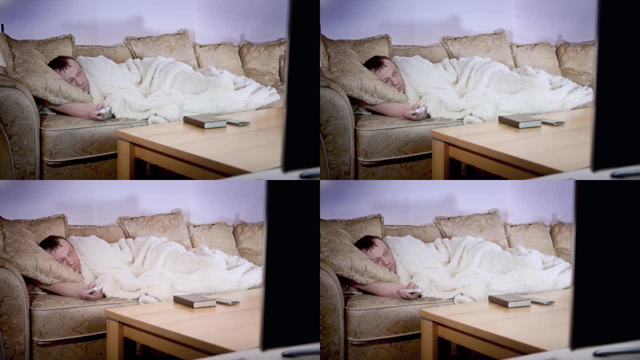 一名男子躺在沙发上盖着毯子，切换电视频道，晚上照明