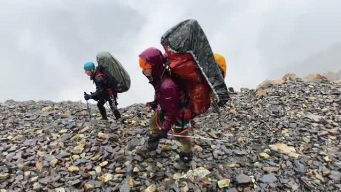 大背包湿透的游客在大雨中走在湿滑的石头上