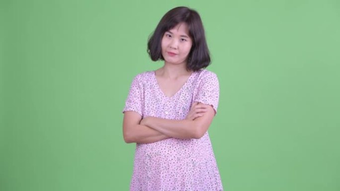美丽的亚洲孕妇微笑的工作室镜头，双臂交叉在绿色工作室背景下