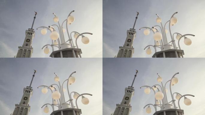 钟塔细节的底部视图和路灯在白天关闭。行动。美丽的塔与一个尖顶和街灯在蓝色多云的天空背景