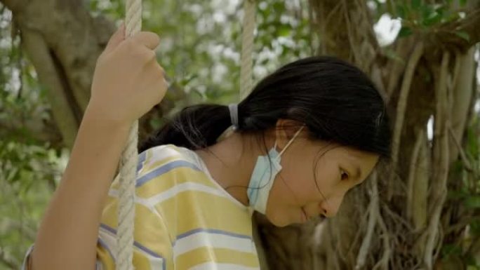 亚洲女孩在户外公园树下玩绳子秋千，生活方式理念。