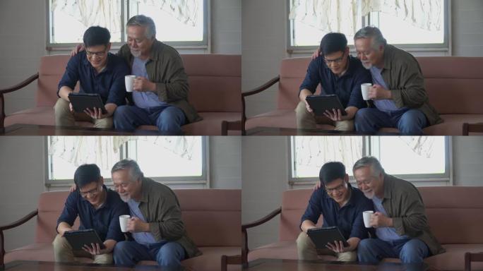 快乐的亚洲小儿子和资深老父亲坐在沙发上一起使用平板电脑在家