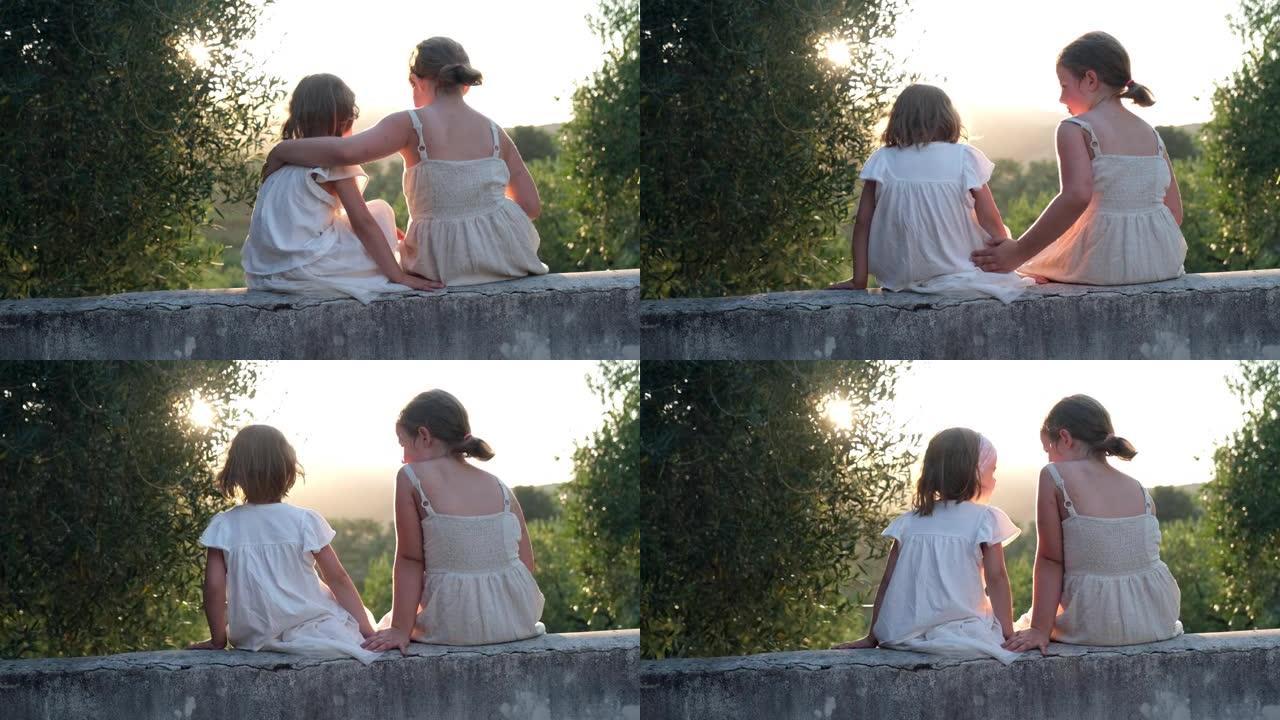 在金色的阳光下，两个年轻的高加索姐妹花时间在坐在托斯卡纳别墅露台墙上时，拥抱和大笑