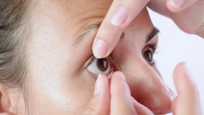 黑发女人拿着手指在眼睛上戴隐形眼镜。治疗眼部疾病，如近视或近视、散光或美容镜片。视力的改善和矫正。