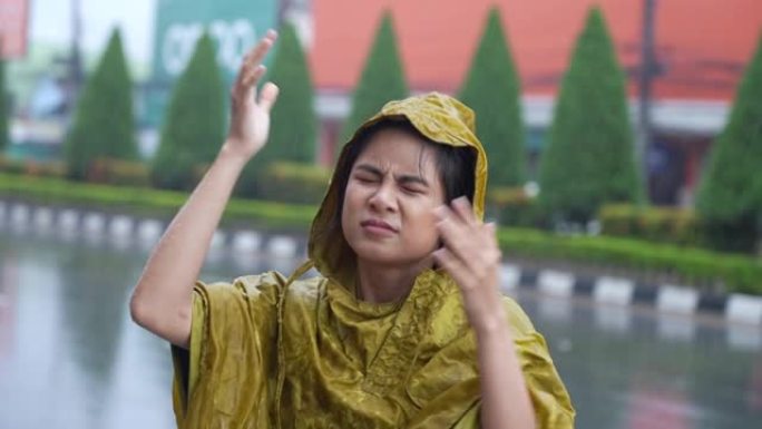 一名穿着雨衣的东亚妇女在街上行走时举手检查倾盆大雨的水平，雨季准备，热带气候变化，在雨中淋湿，