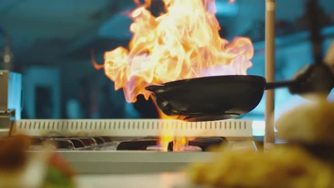 专业厨师烹饪flambe风格。在明火锅中准备盘子肉。厨师在商用厨房的煤气灶上油炸混合食物。男人在餐厅