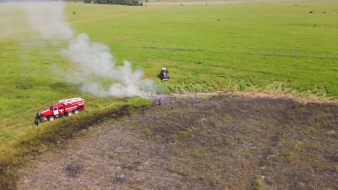 一辆消防车和一辆拖拉机在燃烧的田野边缘冒烟