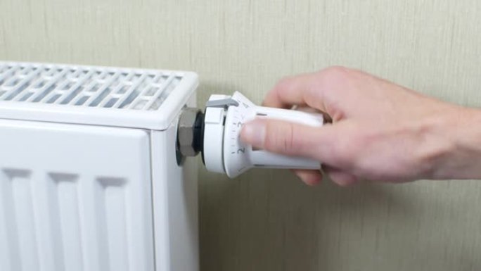 特写，男人的手在家里调节暖气片的旋钮。关闭暖气。散热器暖气的阀门。家庭供暖和保温的概念。
