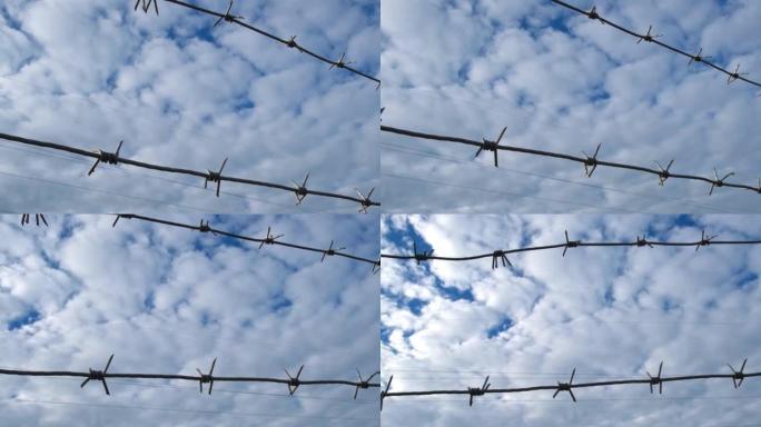 背景上的铁丝网是多云的蓝天。非法移民概念、监狱、监禁、禁区。沿着监狱的铁栅栏慢慢移动。铁丝网围栏。